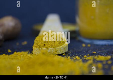 Closeup shot of turmeric yellow powder with a wooden spoon on a dark blue background Stock Photo