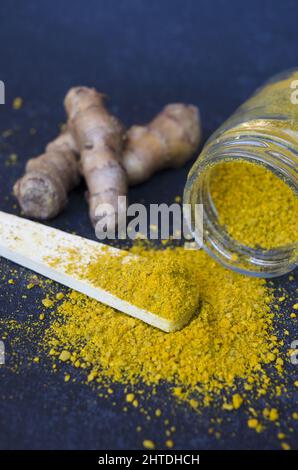 Vertical shot of turmeric jar and roots with a wooden spoon on a dark blue background Stock Photo