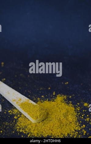 Vertical shot of turmeric yellow powder with a wooden spoon on a dark blue background Stock Photo