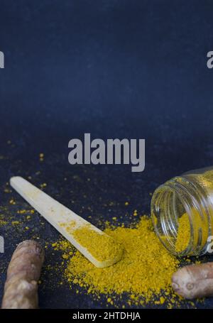 Vertical shot of turmeric jar with a wooden spoon on a dark blue background Stock Photo