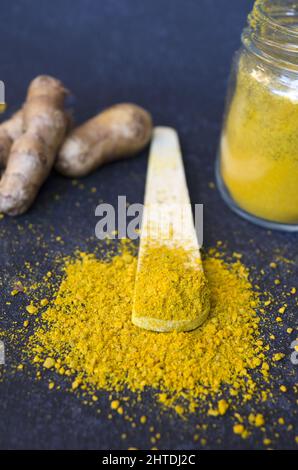 A vertical shot of turmeric jar and roots with a wooden spoon on a dark blue background Stock Photo