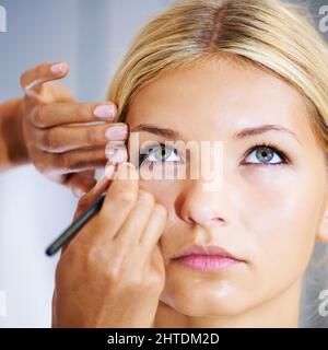 Lining the eye for a dramatic finish. Pretty young woman having her makeup applied by a stylist. Stock Photo