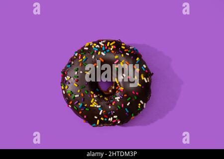 A Donut covered with chocolate and sprinkles on a purple surface. Stock Photo