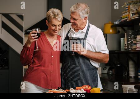 caucasian senior couple drinking wine in kitchen Stock Photo