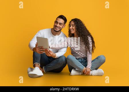 Portrait Of Happy Middle Eastern Couple With Digital Tablet Relaxing On Floor Stock Photo