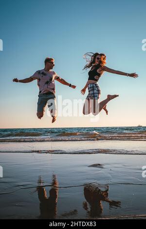 Happy young Caucasian couple jumping on a beach Stock Photo