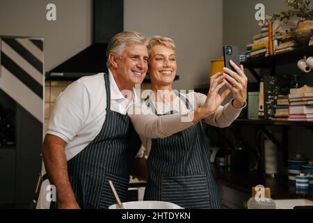 Caucasian senior couple taking selfies in kitchen Stock Photo