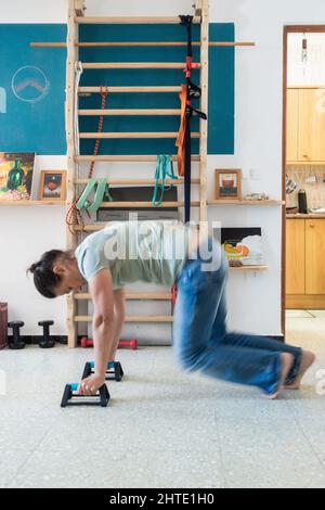 Woman working from home working out at home with homemade wall bars in background. Stock Photo