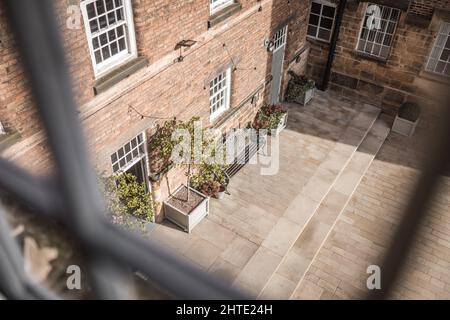 Old mill warehouse red brick courtyard with bench and trees on summer day. Looking out of old wooden sash window. Stock Photo