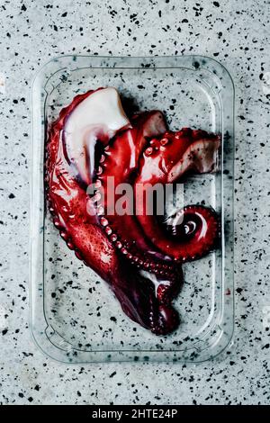 high angle view of some cooked cuts of octopus arms in a plastic tray on a fake granite surface Stock Photo