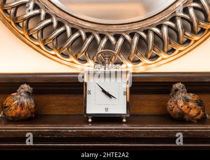 Beautiful old silver carriage clock with mirror and taxidermy stuffed birds either side. Retro vintage style on solid oak wooden mantlepiece. Stock Photo