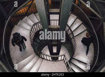Top-view of people walking down the spiral stairs Stock Photo