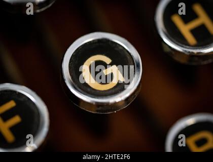 Retro vintage typewriter circular round key closeup with gold coloured letter G on black background. Stock Photo