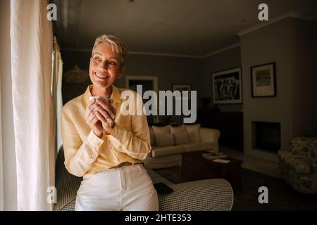 Caucasian senior female holding coffee cup relaxing in living room Stock Photo