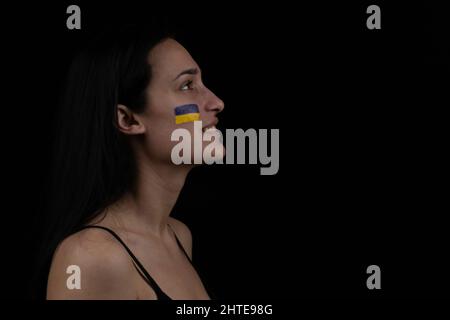 Portrait of beautiful adult Ukrainian woman with yellow blue flag on her face. Patriotism concept. Ukrainian brunette girl on dark background. Space f Stock Photo