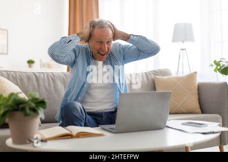 Mature man using laptop celebrating success at home Stock Photo