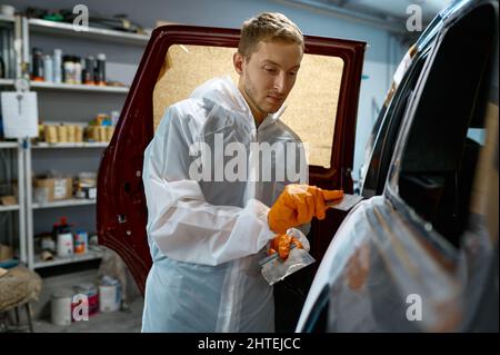 Mechanic puttying plastering car body in garage Stock Photo