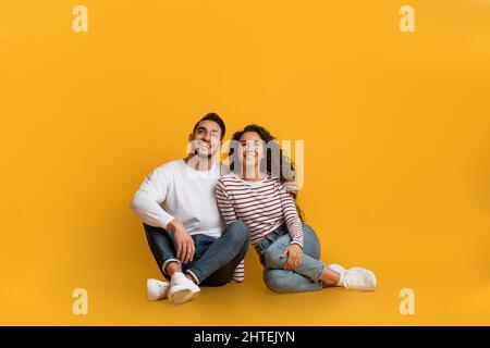 Dreamy Young Arab Couple Sitting On Floor And Looking At Copy Space Stock Photo