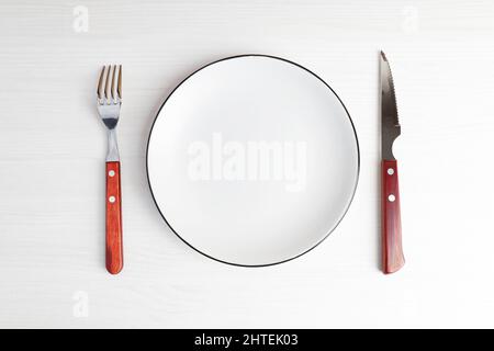 Empty white plate, fork and knife on white wooden table. Top view. Copyspace. Stock Photo