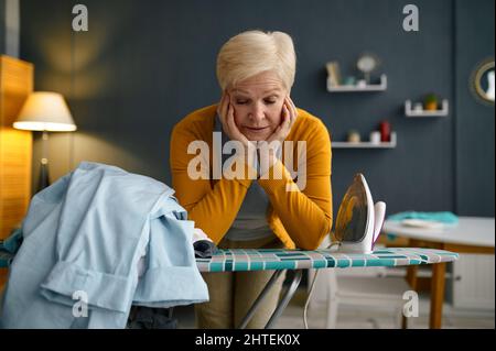Tired old woman front of ironing board Stock Photo