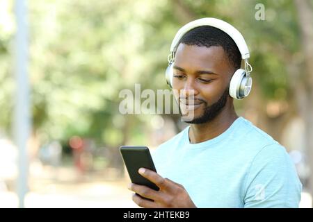 Man with black skin wearing wireless headphones listening to music with phone in park Stock Photo