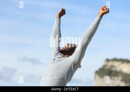 Euphoric man with black skin raising arms celebrating success in nature Stock Photo