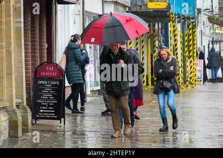 Bridport, Dorset, UK.  28th February 2022.  UK Weather. Shoppers shelter under an umbrella as they walk along the pavement in the heavy rain at Bridport in Dorset on a wet afternoon on the last day of meteorological winter.  Picture Credit: Graham Hunt/Alamy Live News Stock Photo