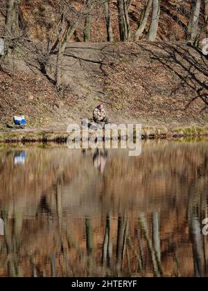 Fisherman on a quiet lakeshore with autumn tree reflections while checking his phone. Stock Photo