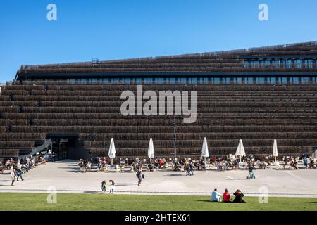 Düsseldorf, Germany - MARCH 2022- Outdoor sunny view people sit on green roof and outdoor cafe at Schadowstraße and background of green modern facade Stock Photo