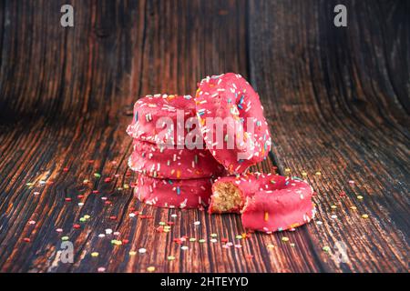 A stack of pink donuts decorated with colorful sprinkles on a wooden background Stock Photo