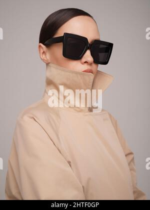 Beautiful young lady in a beige trench coat and black sunglasses. Fashion and style Stock Photo