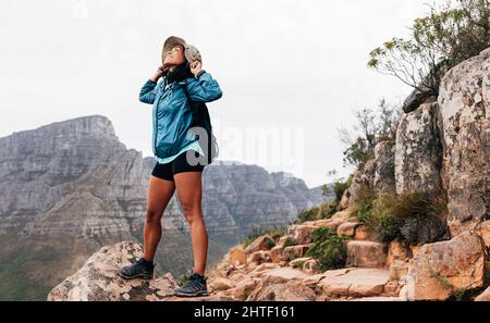 Happy woman hiker holding her hat while looking up standing on a top of a mountain Stock Photo