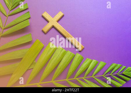 Cross and palm leaves on purple background. Lent season concept. Stock Photo