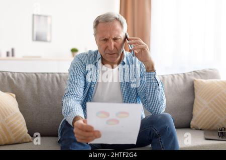 Focused mature man holding paper reading report talking on phone Stock Photo