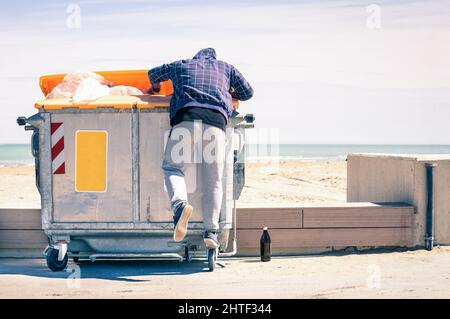Young tramp rummaging in trash container looking for food and reusable goods - Modern concept of poverty with normal citizens becoming suddenly poor - Stock Photo