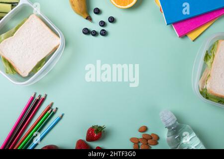 Fruits, sandwiches with color pencils and books on green background with copy space at center Stock Photo