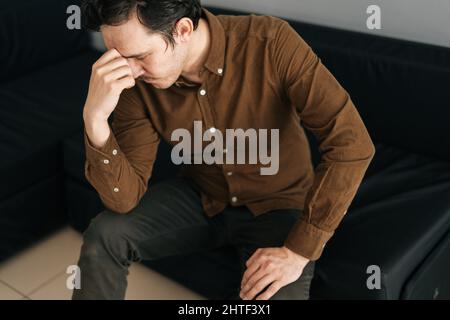 High-angle view of worried young man sitting alone feeling sad worry regret or fear, depressed and desperate in sofa at home. Stock Photo