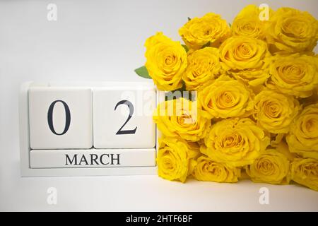 Wooden calendar March 2 and yellow roses on a white background.  Stock Photo