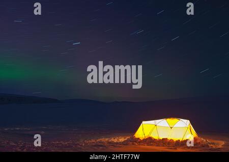 faint northern lights over illuminated tent on Langjokull glacier Stock Photo
