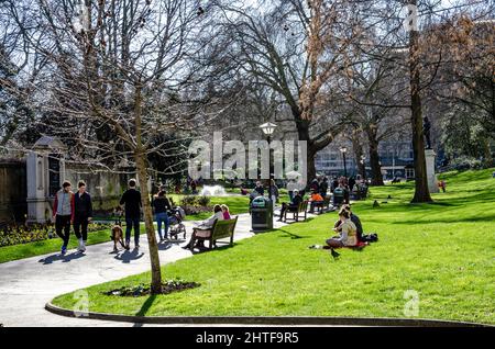 London Memorial Gardens busy with people walking and sat on benches along the main path through the park. Stock Photo