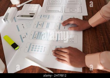 Hands of UX designer leaning on table with layouts of new mobile application interface Stock Photo