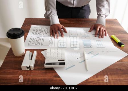 Hands of project manager leaning on table with printed mockups of mobile interface Stock Photo