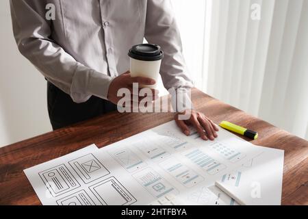 Project manager drinking cup of coffee when checking mobile app templates created by UI and UX designers Stock Photo