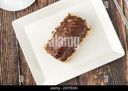 Dessert Cake from Malaga on wooden table. Cake with banana inside, covered with chocolate sauce and hazelnuts. Stock Photo