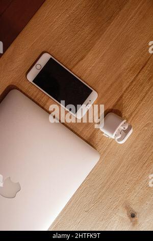 Vertical shot of an iPhone, AirPods and a MacBook Pro displayed on a wooden surface Stock Photo