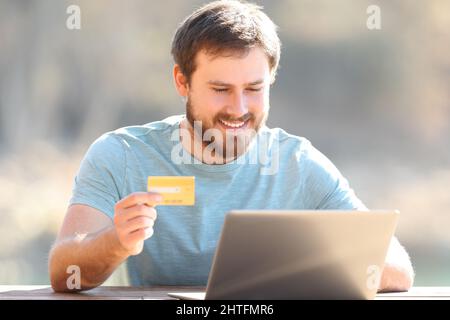 Happy man buying online using credit card and laptop outdoors Stock Photo