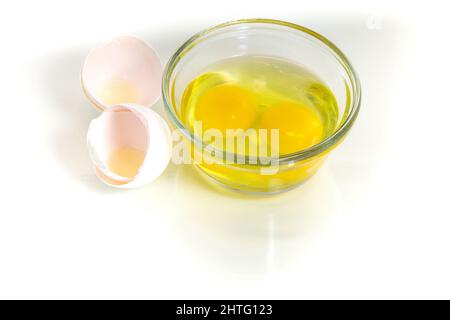Two fresh broken eggs in a glass bowl with broken shell near. Studio shot, white background and copy space. Stock Photo