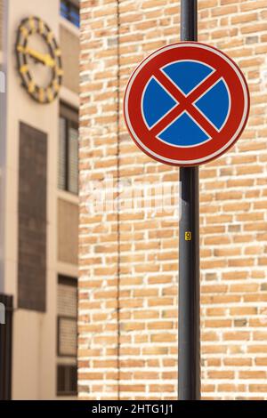 Round traffic sign in front of brick wall and clock with crossed out blue shape meaning it is not allowed to park or even stand still Stock Photo