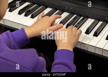 Two hands of a child playing the piano. Selective focus on children's fingers and piano keys for playing the piano. Stock Photo