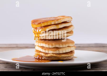 Stack of eight pancakes with syrup served in plate on table against gray background Stock Photo